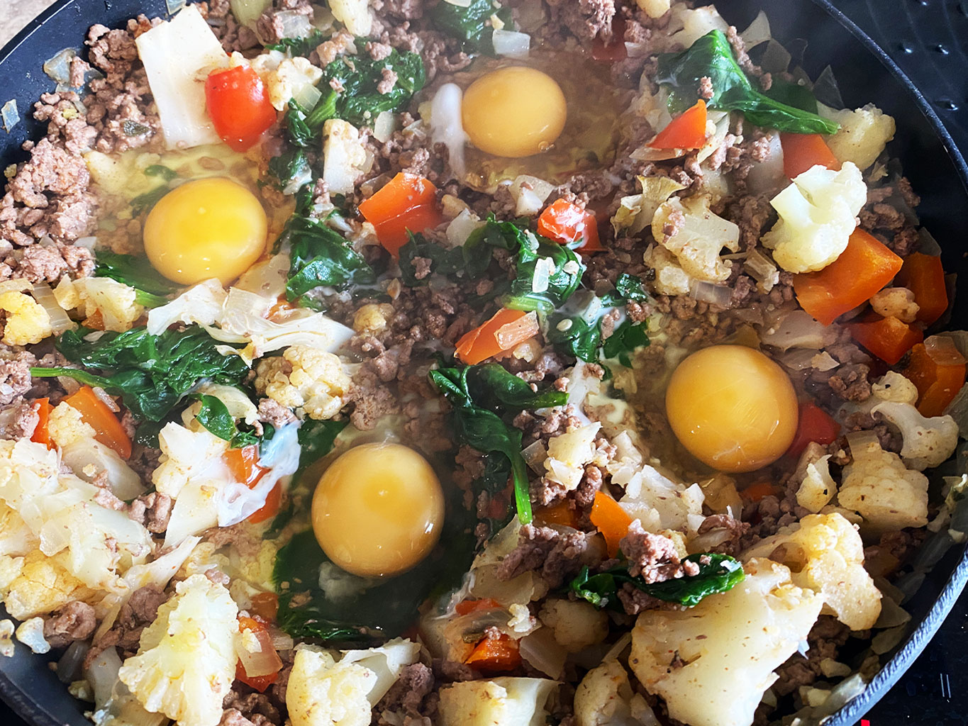 Eggs poaching in ground beef and veggie scramble